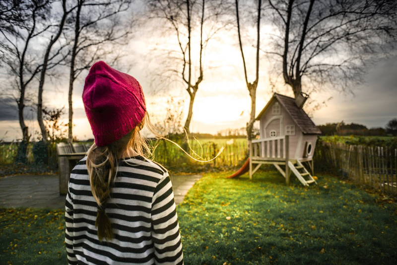 Girl standing in front of a small treehouse on the ground in a backyard.