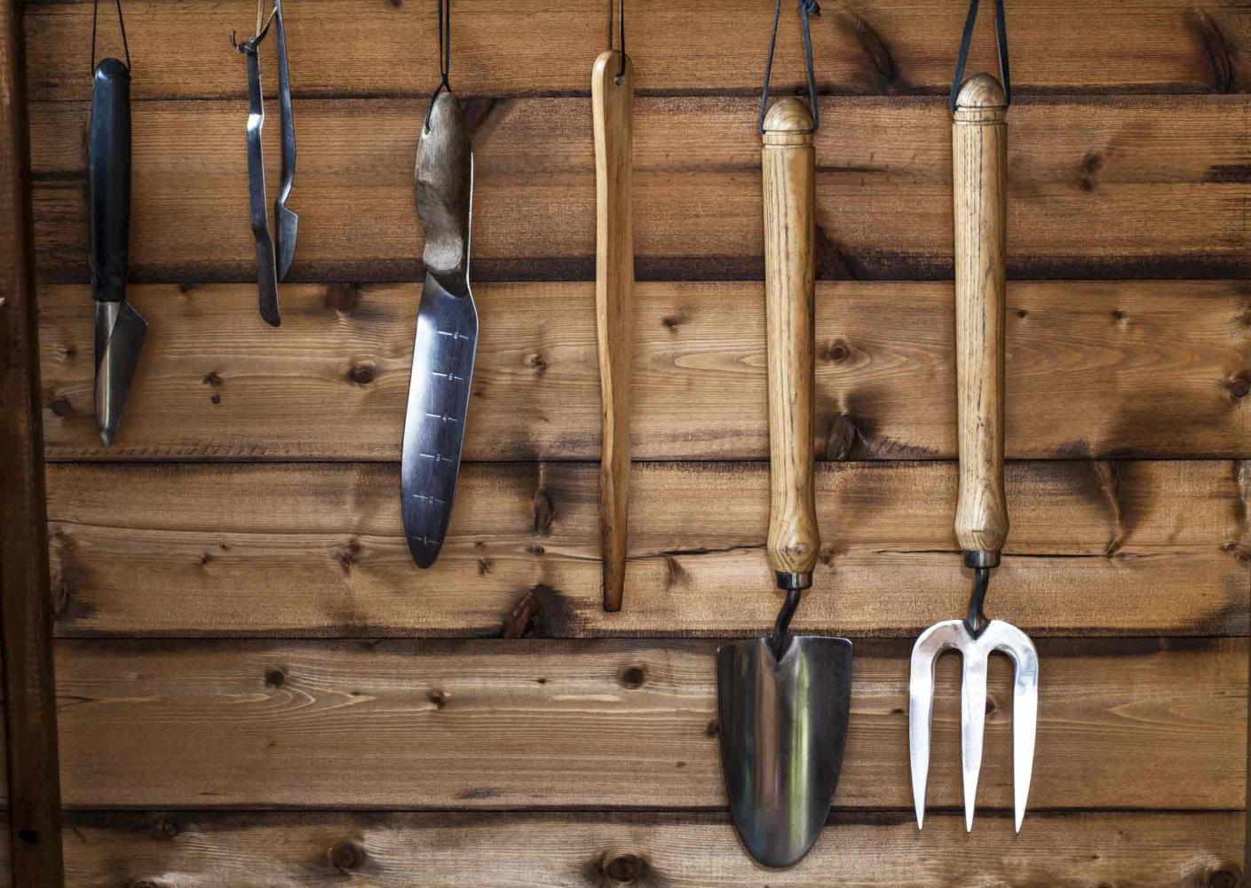 Close up of gardening tools hanging on a wooden wall.