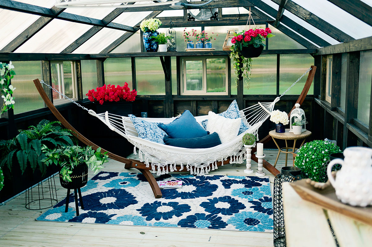 Interior of a Yoderbilt Greenhouse with gray stain. A hammock and vibrant plants surrounding are inside.