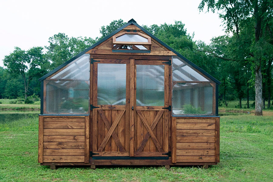 Front exterior view of a 12x20 Yoderbilt Legacy Greenhouse with brown stain. Double doors are closed.