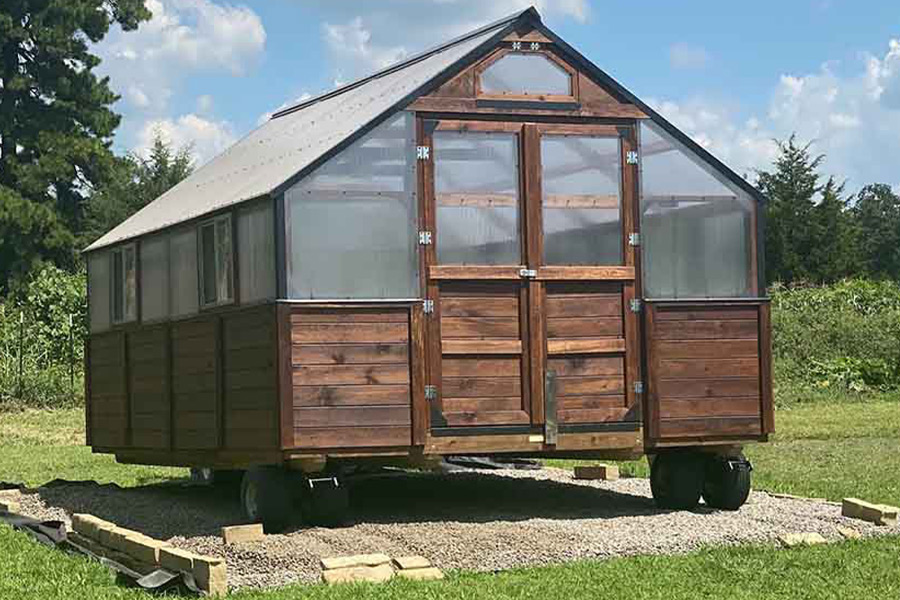 Exterior view of a brown stain Yoderbilt Legacy Greenhouse with double doors being installed on wheels.