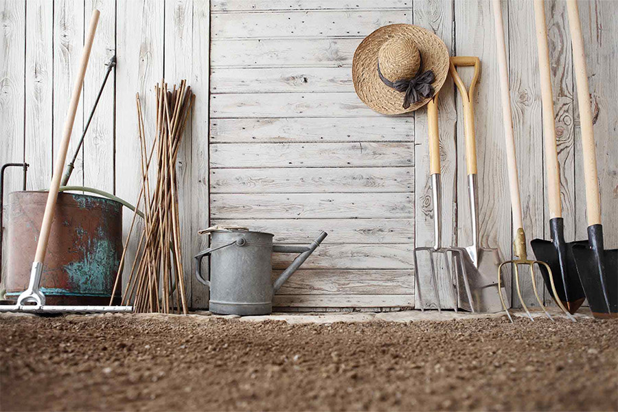 Close up of several gardening tools in front of a wooden wall.