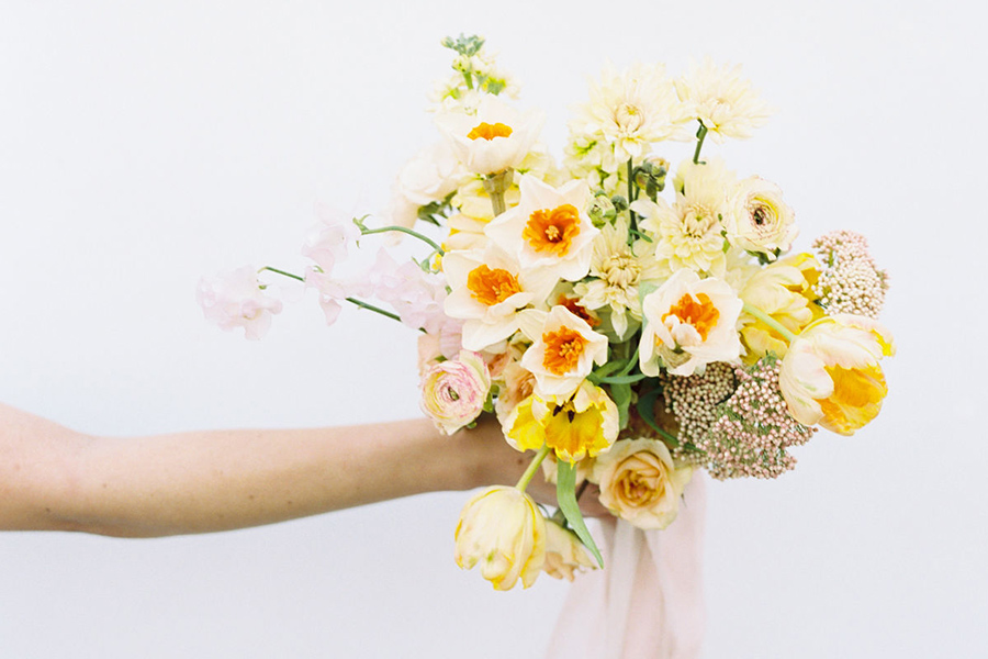 Hand holding a bouquet of various yellow flowers.