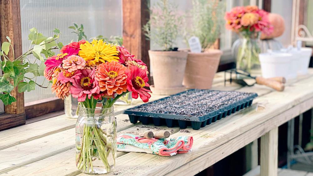 Vase of flowers and gardening tools on a wooden bench in a Yoderbilt Greenhouse.