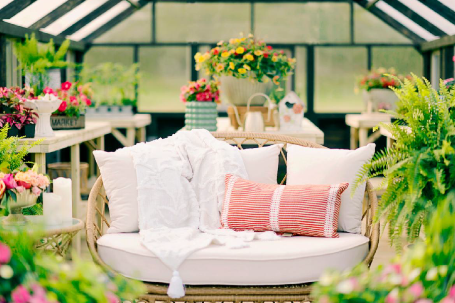 Interior of a Yoderbilt Greenhouse with gray stain with a white couch and various plants on wooden benches.