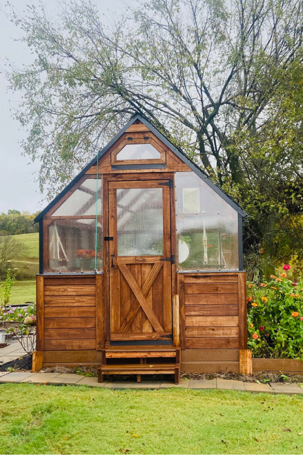 Exterior view of a Yoderbilt Greenhouse with brown stain with a single door.