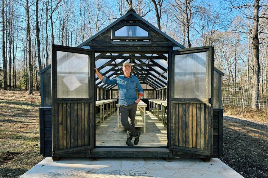 Joe Lamp'l standing in the doorway of his Yoderbilt greenhouse with gray stain.