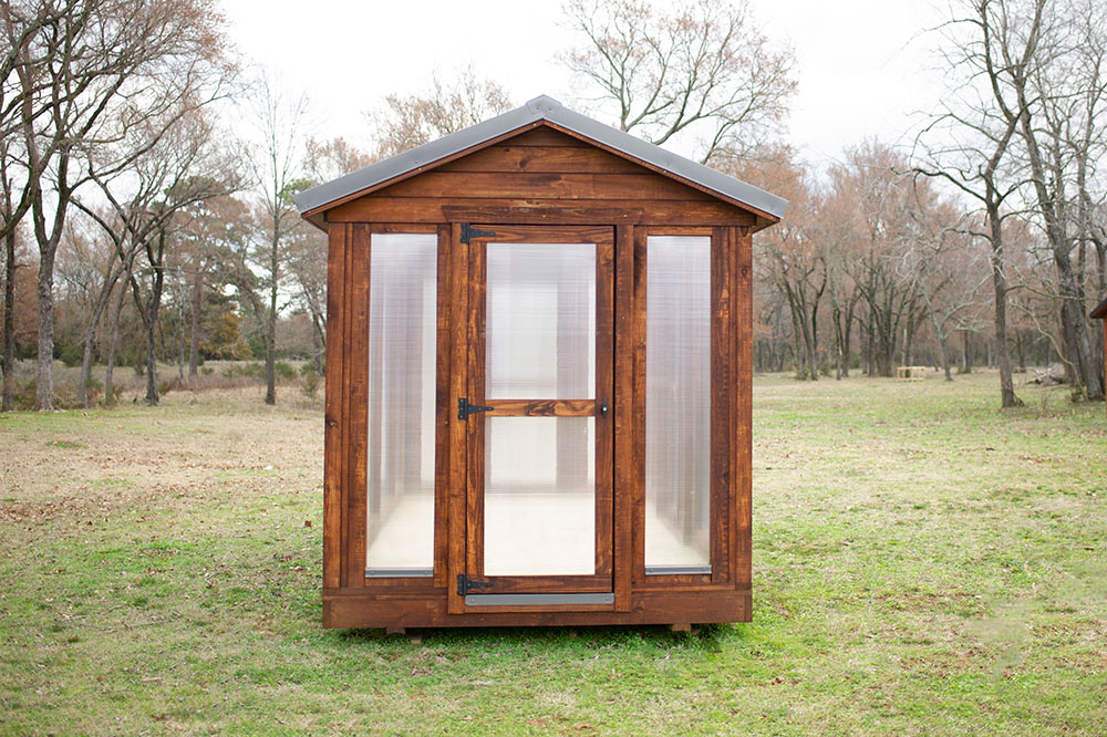 Front exterior view of an 8x16 Yoderbilt Traditional Greenhouse with brown stain and a single door.