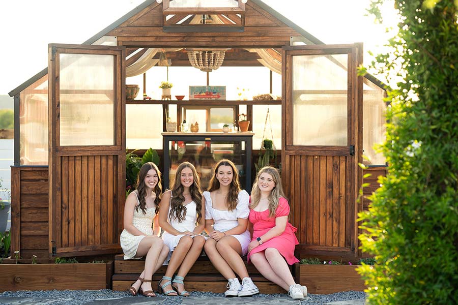Four teenage girls sitting in the entrance of a Yoderbilt Greenhouse posing