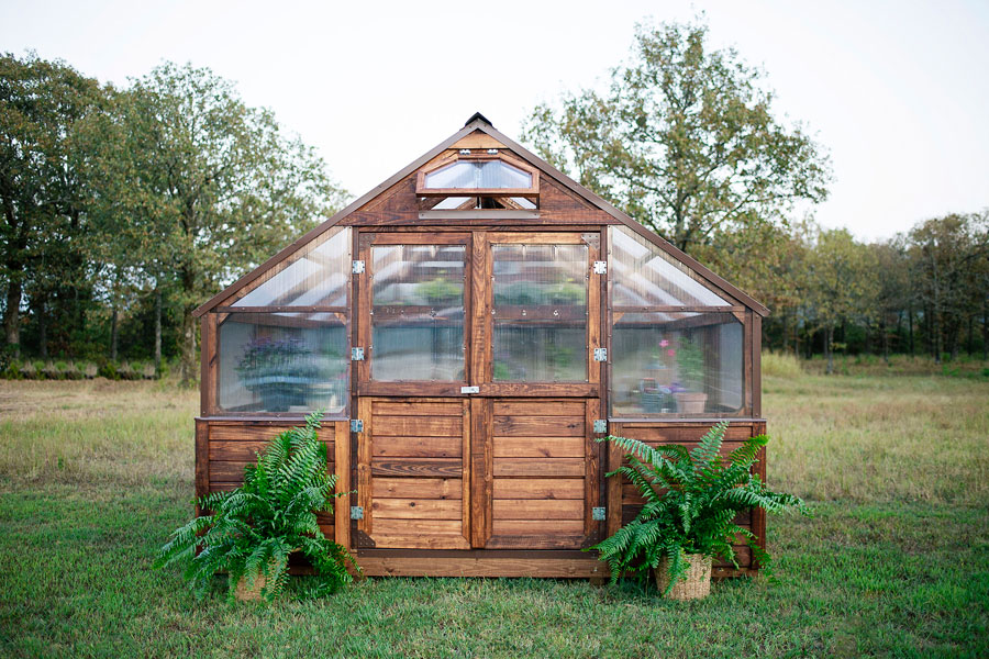 Outside shot of a 12x12 Yoderbilt Legacy Greenhouse with two plants on each side of the door.