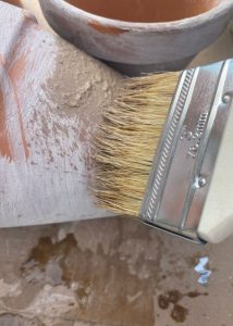 A terra cotta pot being brushed with another coat of water and garden lime mixture