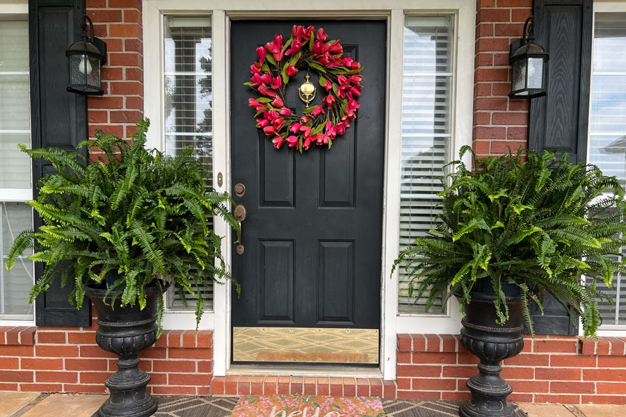 Outside shot of a front porch with two pots with ferns on the left and right.