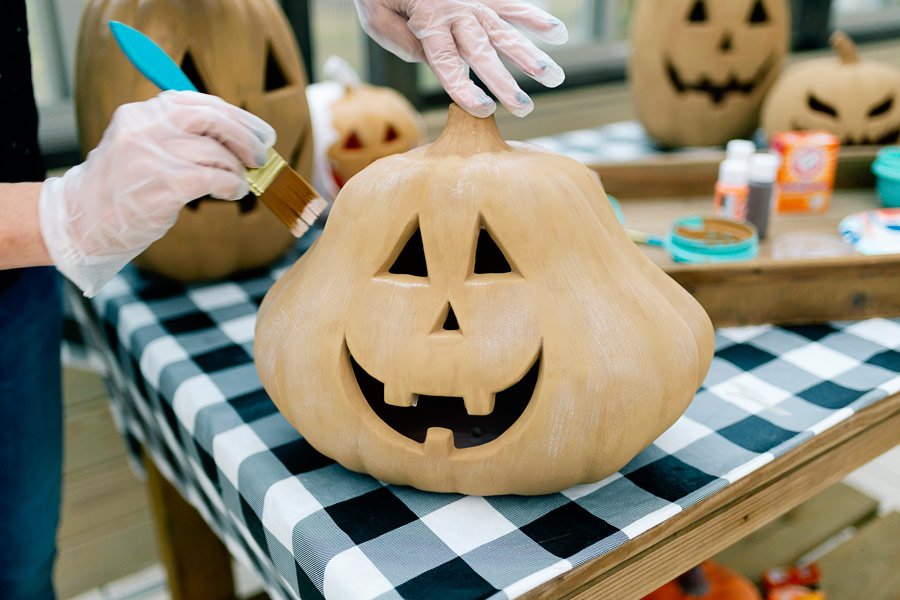 Angela Yoder applying a thin white paint wash over the dried terra cotta pumpkin