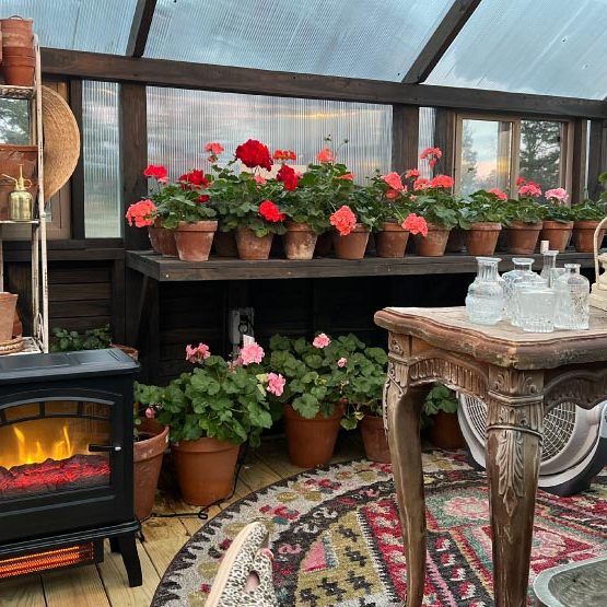 Interior photo of a Yoderbilt greenhouse with brown stain with the wall lined with flowers, a portable fireplace and table.